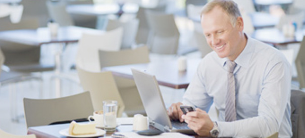 photo of man at table with laptop looking at smartphone